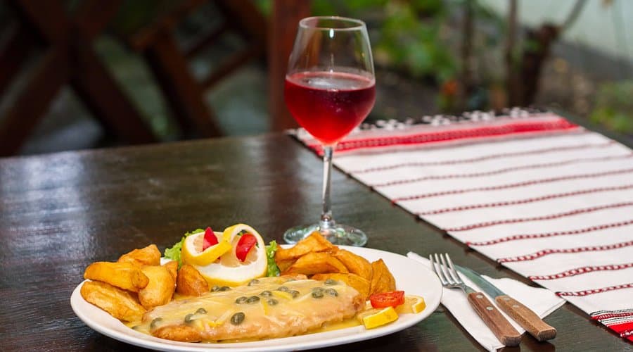 Fel principal cu sos și cartofi, alături de un pahar de vin roșu